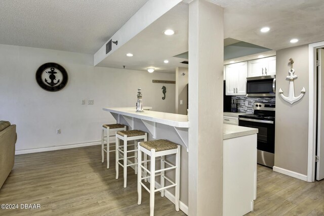 kitchen with decorative backsplash, a breakfast bar, stainless steel appliances, light hardwood / wood-style flooring, and white cabinets