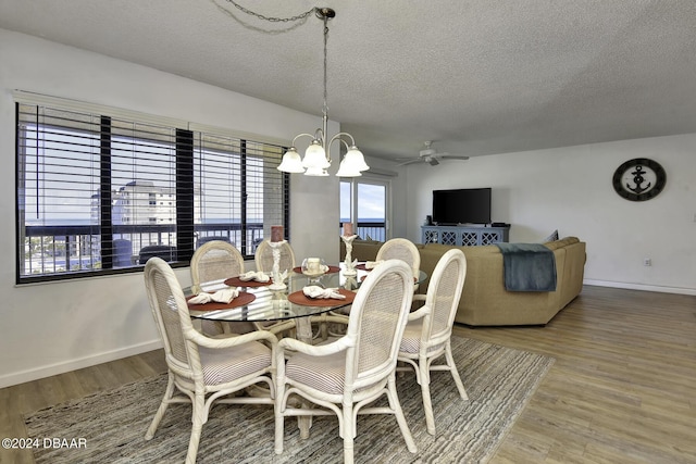 dining area with hardwood / wood-style floors, ceiling fan with notable chandelier, and a textured ceiling