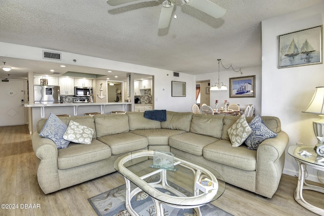 living room with ceiling fan with notable chandelier, a textured ceiling, and light hardwood / wood-style flooring