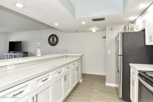 kitchen with a skylight, stainless steel fridge, range with electric stovetop, light wood-type flooring, and white cabinetry