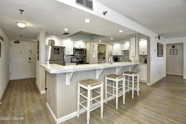 kitchen featuring decorative backsplash, white cabinetry, stainless steel appliances, and a breakfast bar area