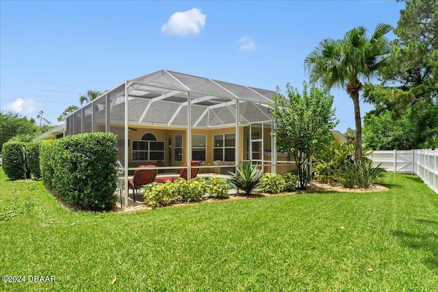 rear view of property featuring a patio, glass enclosure, and a lawn