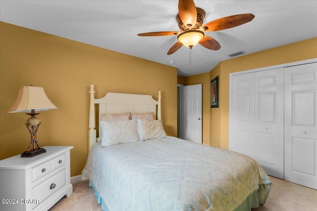 bedroom featuring a textured ceiling, light colored carpet, ceiling fan, and a closet