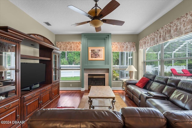 living room with dark hardwood / wood-style flooring, a textured ceiling, a tile fireplace, and ceiling fan