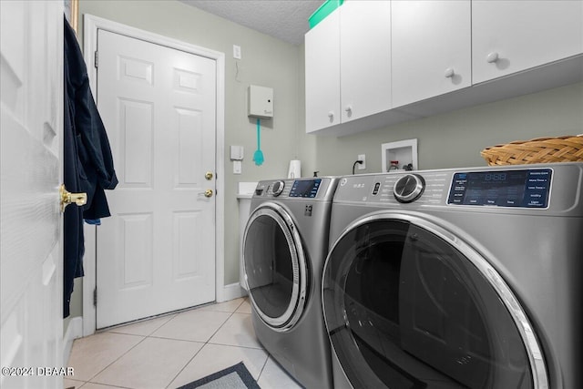 laundry area featuring light tile patterned flooring, a textured ceiling, cabinets, and washer and dryer