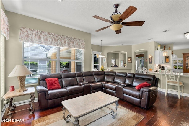 living room featuring dark wood-type flooring, ceiling fan, and a textured ceiling