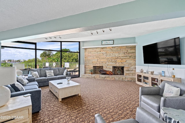 carpeted living room featuring wainscoting, a textured ceiling, and a stone fireplace