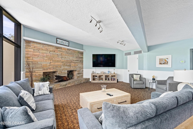 living area featuring wainscoting, visible vents, a textured ceiling, and a stone fireplace