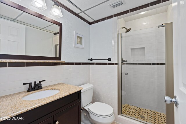 bathroom with tile walls, visible vents, toilet, a shower stall, and vanity