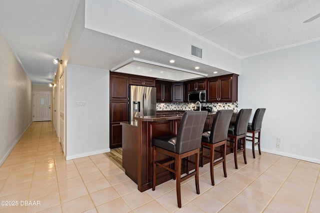 kitchen featuring a breakfast bar area, a peninsula, visible vents, appliances with stainless steel finishes, and backsplash