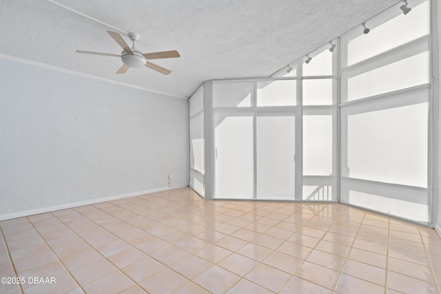 tiled empty room with a ceiling fan, a wealth of natural light, crown molding, and track lighting