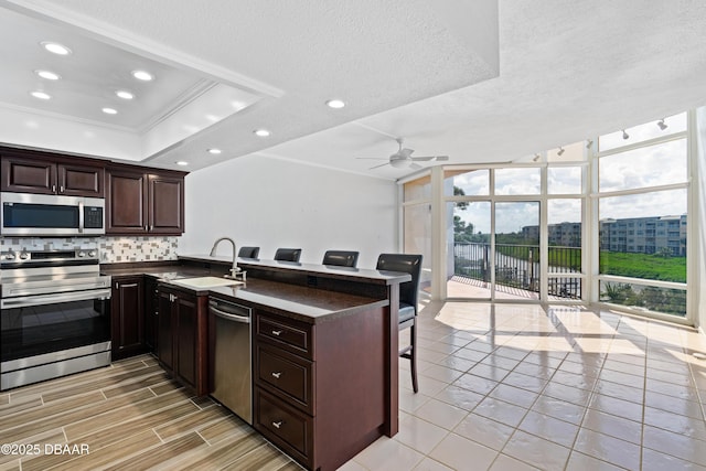 kitchen featuring decorative backsplash, dark countertops, stainless steel appliances, a wall of windows, and a sink