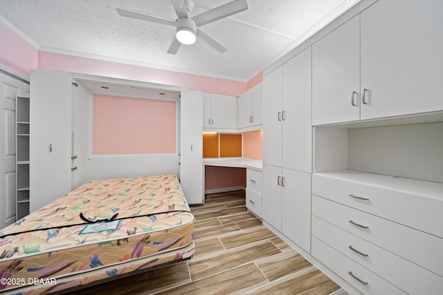 bedroom featuring a textured ceiling, wood finish floors, a ceiling fan, built in study area, and crown molding