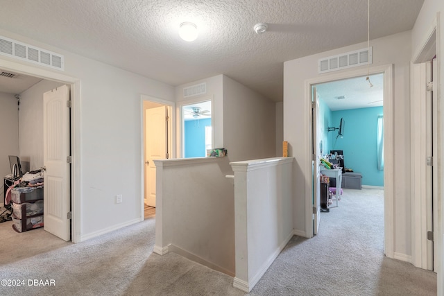 hallway with a textured ceiling and light carpet