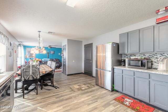 kitchen featuring pendant lighting, light wood-type flooring, appliances with stainless steel finishes, and backsplash