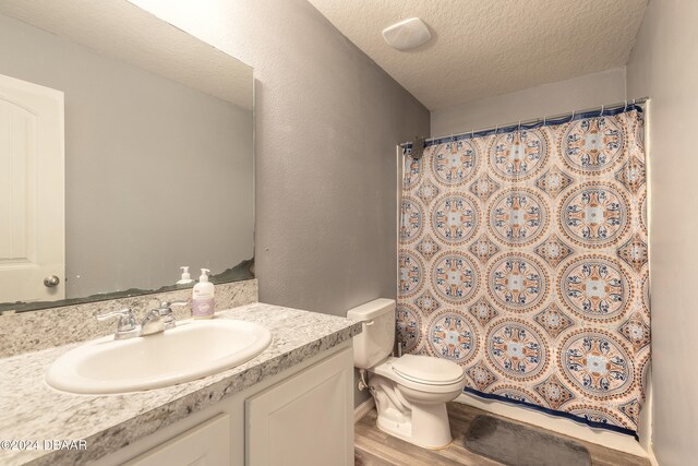 bathroom with a shower with shower curtain, a textured ceiling, wood-type flooring, vanity, and toilet