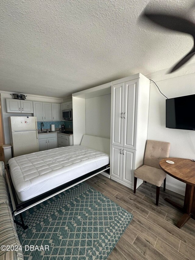 bedroom featuring sink, white refrigerator, a textured ceiling, and hardwood / wood-style flooring