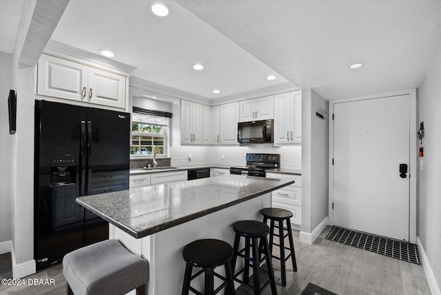 kitchen featuring dark stone counters, a breakfast bar, sink, black appliances, and white cabinets