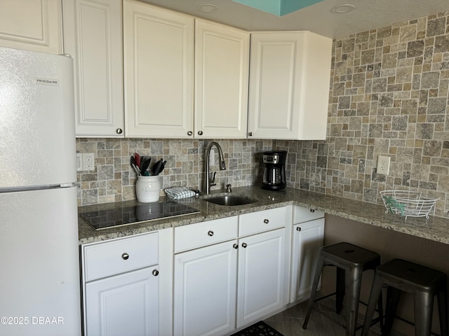 kitchen featuring sink, white cabinets, backsplash, white refrigerator, and black electric cooktop