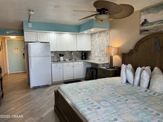 bedroom featuring white refrigerator, sink, light hardwood / wood-style flooring, and a textured ceiling