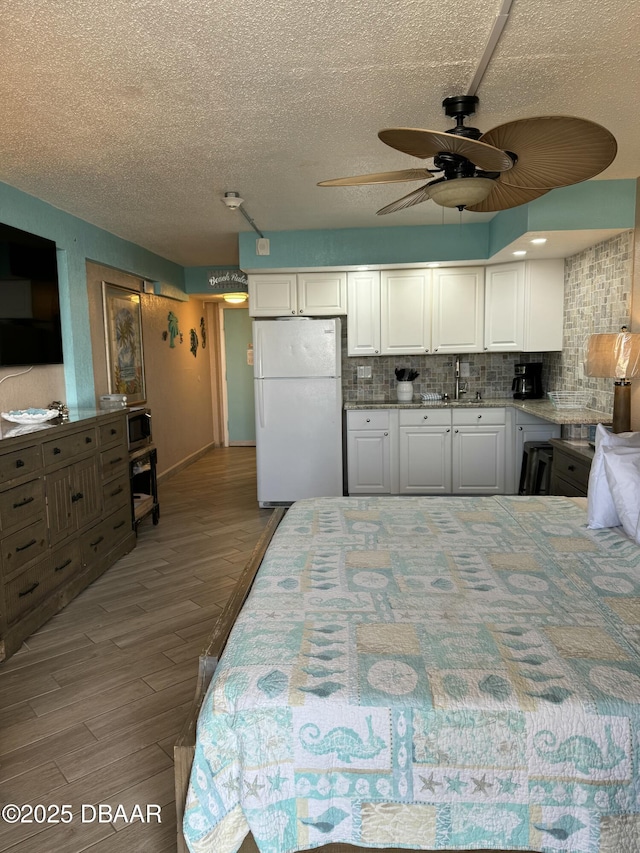 bedroom featuring hardwood / wood-style flooring, white fridge, sink, and a textured ceiling