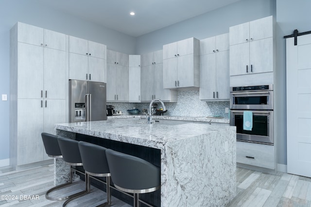 kitchen featuring light hardwood / wood-style flooring, a barn door, a kitchen island with sink, a kitchen breakfast bar, and appliances with stainless steel finishes