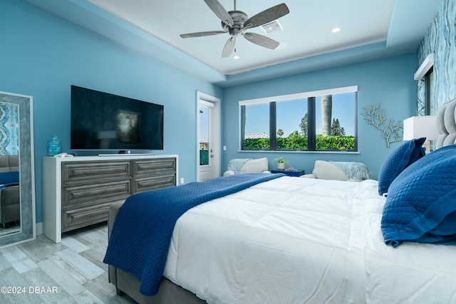 bedroom with ceiling fan, a raised ceiling, and light wood-type flooring