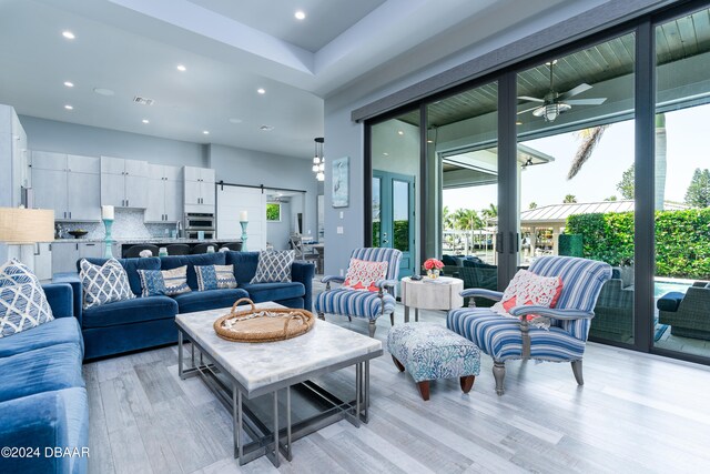 living room with a barn door, light hardwood / wood-style floors, ceiling fan, and french doors