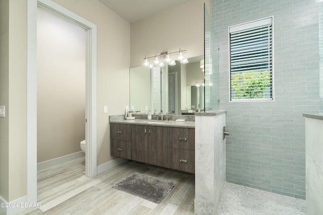 bathroom with wood-type flooring, vanity, a shower, toilet, and tile walls