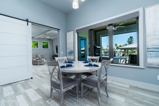 dining area featuring a barn door, beamed ceiling, light hardwood / wood-style flooring, and ceiling fan