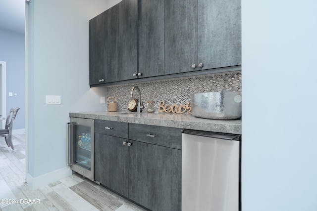 bar with tasteful backsplash, stainless steel refrigerator, sink, light hardwood / wood-style floors, and beverage cooler