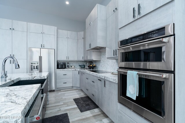 kitchen featuring sink, appliances with stainless steel finishes, light stone countertops, light hardwood / wood-style flooring, and decorative backsplash