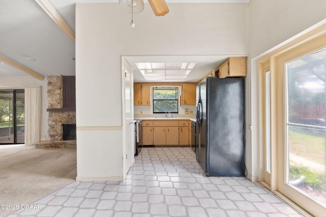 kitchen with a stone fireplace, a sink, light countertops, black fridge, and light floors