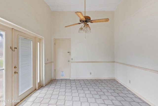 spare room featuring a ceiling fan, baseboards, a towering ceiling, and light floors