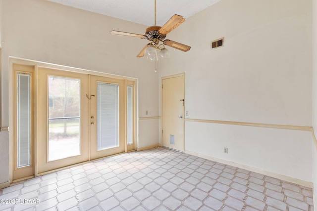 empty room with baseboards, visible vents, a ceiling fan, a high ceiling, and light floors