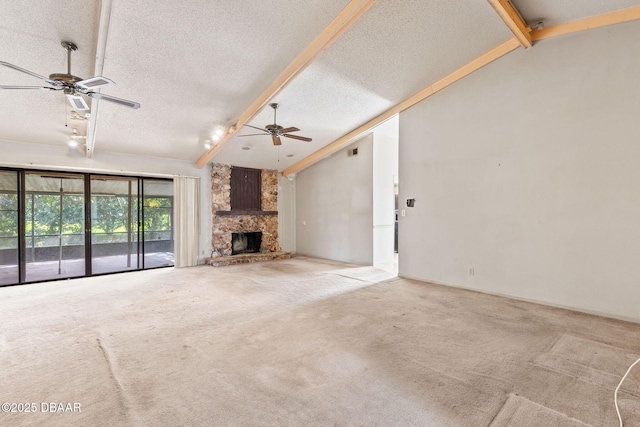 unfurnished living room featuring lofted ceiling with beams, ceiling fan, a stone fireplace, a textured ceiling, and carpet flooring