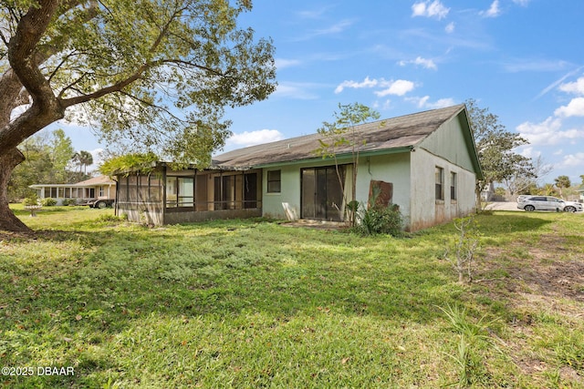 rear view of house with a yard, a sunroom, and stucco siding