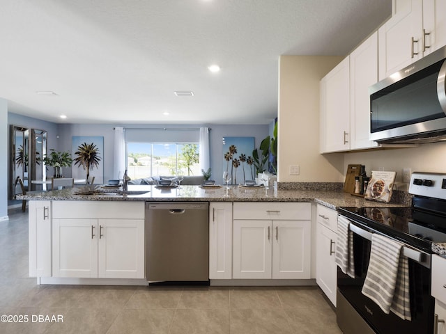 kitchen with sink, white cabinetry, dark stone countertops, kitchen peninsula, and stainless steel appliances