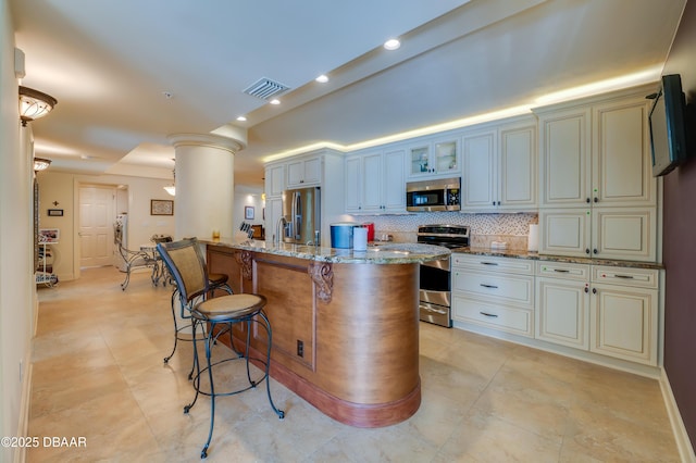 kitchen with backsplash, a kitchen bar, light stone counters, stainless steel appliances, and cream cabinets