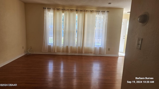 spare room featuring a textured ceiling, a wealth of natural light, and dark hardwood / wood-style floors