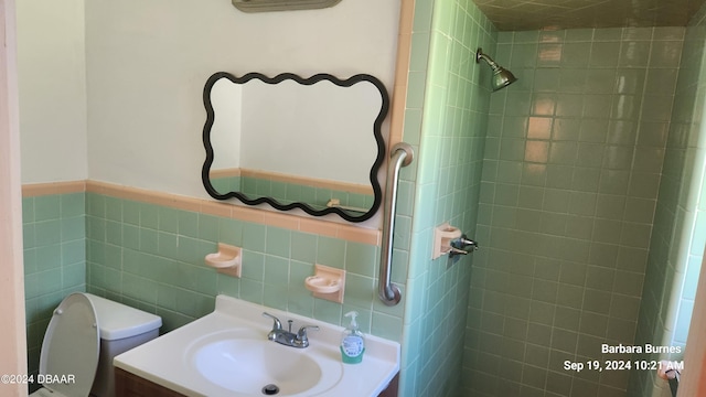 bathroom with toilet, vanity, a tile shower, and tile walls