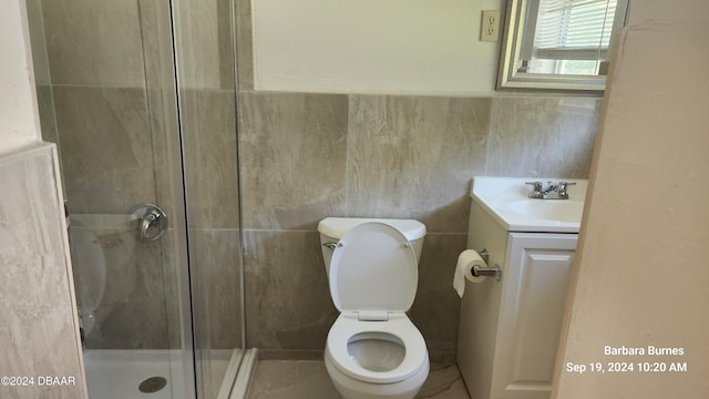 bathroom with a shower with shower door, vanity, toilet, and tile walls