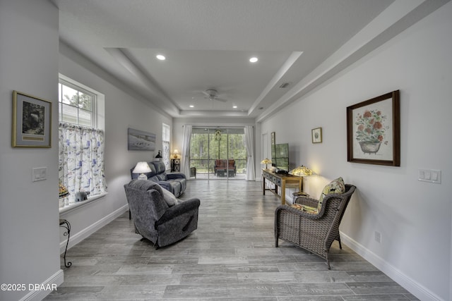 living area featuring wood finished floors, baseboards, recessed lighting, a tray ceiling, and a ceiling fan