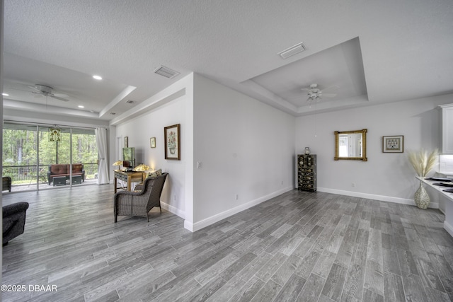 living room featuring baseboards, a tray ceiling, visible vents, and ceiling fan