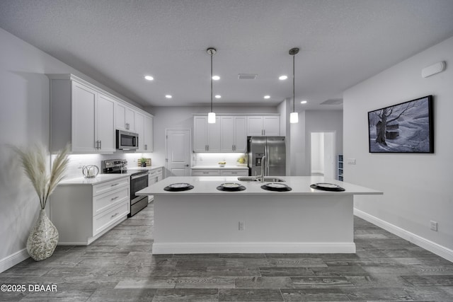 kitchen with dark wood-style flooring, appliances with stainless steel finishes, a kitchen island with sink, white cabinetry, and visible vents