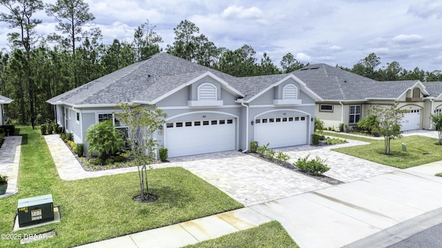 view of front of property featuring roof with shingles, an attached garage, stucco siding, a front yard, and decorative driveway