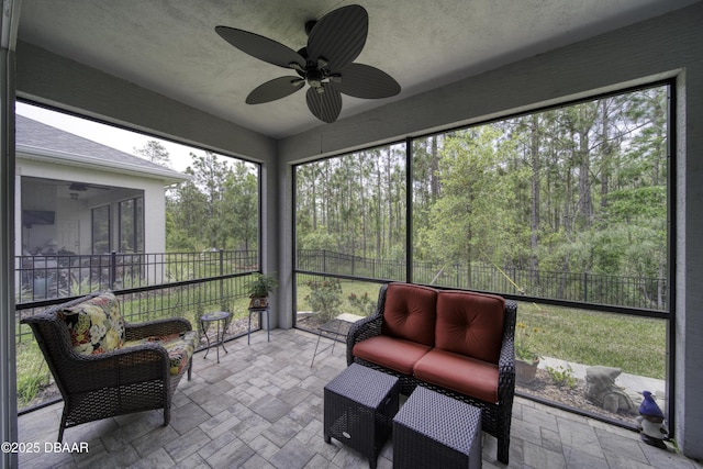 sunroom featuring a ceiling fan and a forest view