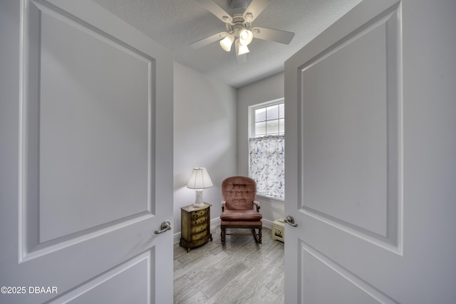living area featuring light wood-style floors, baseboards, ceiling fan, and a textured ceiling