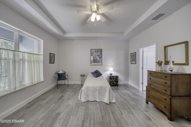 bedroom with visible vents, a raised ceiling, baseboards, and light wood-type flooring