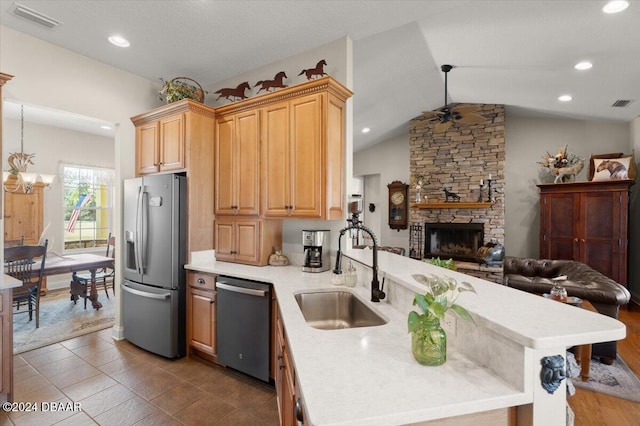 kitchen with pendant lighting, lofted ceiling, sink, appliances with stainless steel finishes, and kitchen peninsula